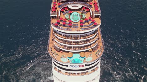 A-drone-flies-up-to-the-Carnival-Panorama-cruise-ship-stern-full-of-patio-umbrellas-and-tourists-while-anchored-in-the-bay-of-Cabo-San-Lucas,-Mexico