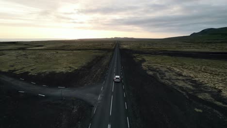 Panoramic-aerial-view-of-a-car-driving-on-a-lave-fields-endless-road,-Iceland