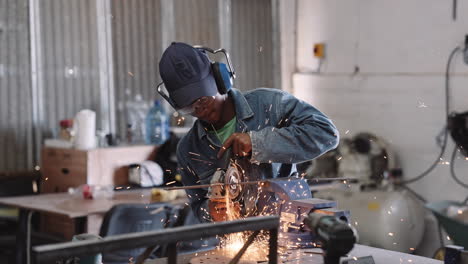 Slow-motion-track-right-of-young-black-male-working-angle-grinder-power-tool-in-workshop-with-sparks-in-circular-spray