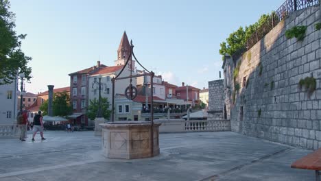 Ein-Brunnen-Auf-Dem-Fünf-Brunnen-Platz-Und-Fußgängern,-Im-Hintergrund-Der-Kirchturm