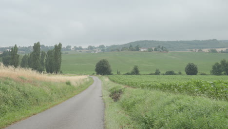 A-quiet-country-road-in-southern-France-surrounded-by-rolling-hills,-vineyards-and-farmland-on-a-cloudy-summers-day