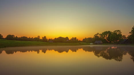 The-setting-sun-reflecting-off-the-still-misty-surface-of-a-countryside-lake---sunset-to-nighttime-time-lapse