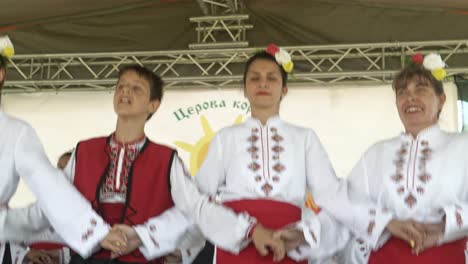 Lächelnde-Menschen-Tanzen-Auf-Der-Bühne-Des-Kulturellen-Volksfestivals-Traditionelles-Horo