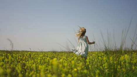 Young-blonde-girl-in-white-dress-runs-through-tall-grass-and-flower-field-happy