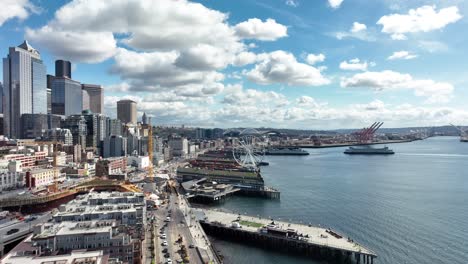 Establishing-shot-of-Seattle-Waterfont-over-Elliott-Bay-with-the-Great-Wheel,-aerial-in-cloudy-blue-skies
