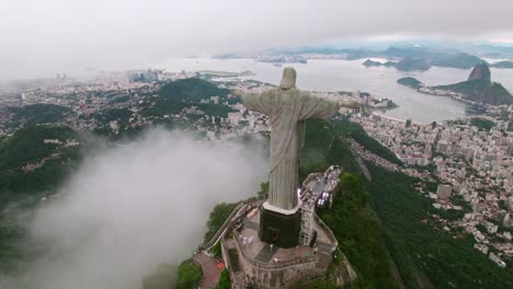 Aerial-orbit-of-Christ-the-Redeemer-Rio-de-Janeiro-Brazil-people-visiting,-Guanabara-bay-cloudy-day