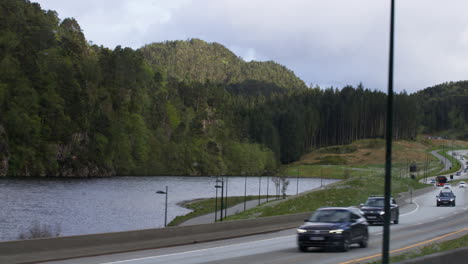 Hand-held-shot-of-cars-passing-past-a-small-lake-in-the-countryside-of-Vestland