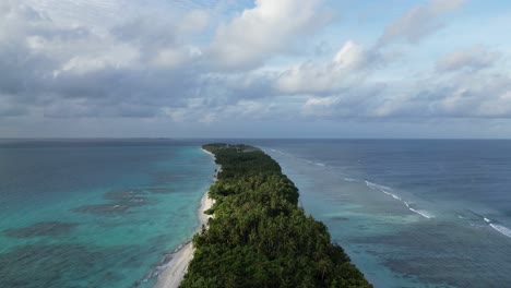 Vertical-aerial-along-Dhigurah-island-in-the-Maldives,-a-long-sandbank-covered-in-lush-tropical-vegetation-of-coconut-palm-trees
