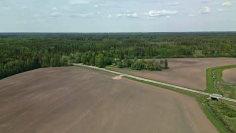 road-going-into-the-woods-surrounded-by-bare-land,-aerial-tilting-up