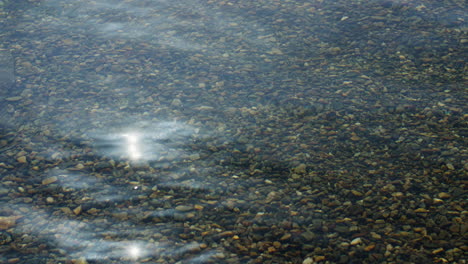 Static-shot-of-crystal-clear-water-with-small-pebbles-below-with-the-sun-reflecting