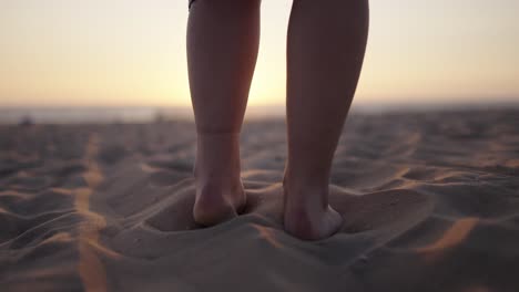 Closeup-tracking-follow-of-woman-in-dress-walking-towards-sunset-on-sandy-beach
