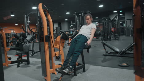 Weitwinkelaufnahme-20er-Jahre-Männer-Beim-Training-Sitzender-Rückenverlängerungsmaschine-Orangefarbenes-Indoor-Fitnessstudio