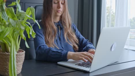 Young-Caucasian-woman-working-on-a-laptop-in-a-modern-grey-office,-in-Slow-Motion