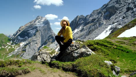 A-woman-resting-on-a-rocky-stone,-enjoying-a-sunny-day-with-the-mountain-rocks-in-the-background