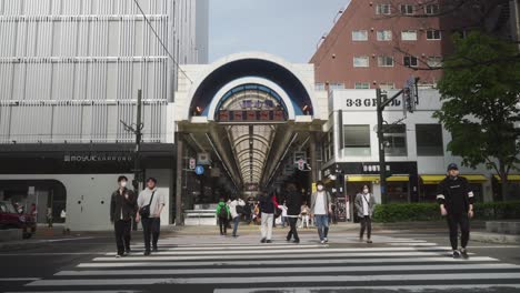 Japanese-Locals-Walking-Over-Crosswalk-Towards-Entrance-To-Tanukikoji-Shopping-Arcade