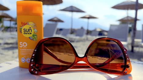 Closeup-of-sunglasses-and-sunscreen-placed-on-a-beach-table