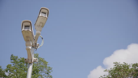 Upwards-shot-of-two-CCTV-security-cameras-against-blue-sky,-copy-space-right