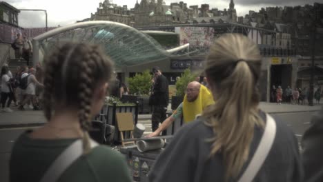 Witness-an-extraordinary-man-performing-a-captivating-balancing-act-and-then-stepping-down-in-the-vibrant-city-of-Edinburgh,-captivating-a-crowd-as-two-girls-watch-in-the-foreground