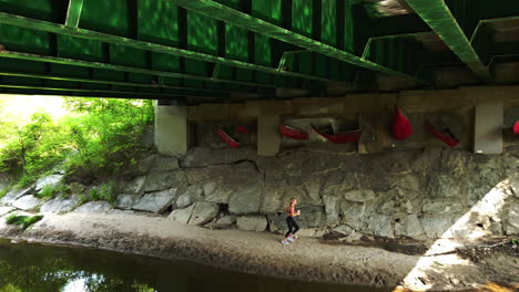 Wide-shot-of-female-jogger-passing-by-red-canoe-installation-underneath-a-bridge