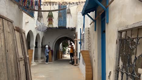 FPV-Caminando-Por-El-Mercado-De-Houmt-Souk-Serpentea-Mientras-Una-Mujer-Toma-Una-Fotografía-Del-Hombre,-Isla-De-Djerba-En-Túnez