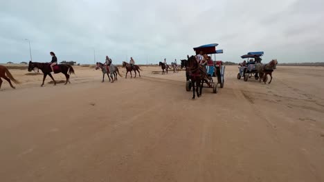 Reverse-tracking-shot-of-horse-caravan-pulling-carriages-and-tourists-on-horseback-crossing-Djerba-desert-in-Tunisia