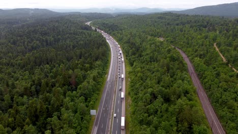 Vehicles-on-a-highway-starting-to-form-two-lanes-due-to-congestion-and-traffic-accident-in-small-European-country-with-national-road-between-tall-trees