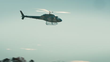 Wide-shot-of-a-helicopter-flying-against-a-blue-sky-and-forested-background