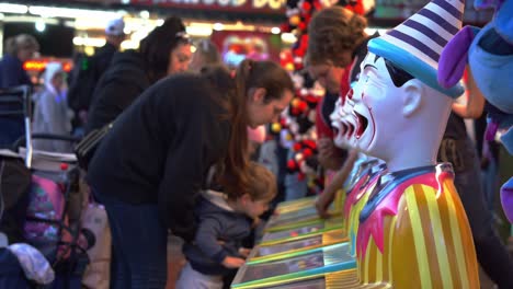 Mother-holding-a-kid-up-to-drop-the-ball-in-laughing-clowns'-mouth,-popular-carnival-games-at-Ekka-Brisbane-Showgrounds,-iconic-annual-festival-Royal-Queensland-Show,-Australia,-handheld-motion-shot