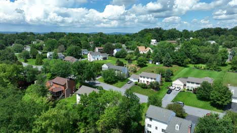 Descending-drone-shot-off-American-rural-neighborhood-with-green-trees-and-puffy-clouds-at-sky