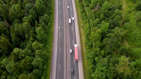 Bird-eye-view-of-European-highway-with-nice-traffic-flow-cars-and-trucks-in-the-middle-of-summer-with-national-road-in-the-green-belt-between-tall-trees
