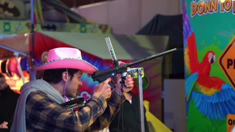 Man-with-iconic-pink-cowboy-hat-playing-carnival-shooting-gallery-game-with-recreational-guns-loaded-with-silicon-rubber-balls-at-iconic-Ekka,-Royal-Queensland-Show-at-Brisbane-Showgrounds