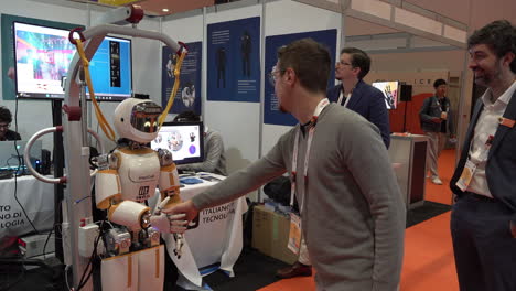 A-man-shakes-hands-with-a-humanoid-robot-and-hands-it-a-cardboard-box-at-the-IEEE-Robotics-and-Automation-Society-Conference-at-the-Excel-Centre