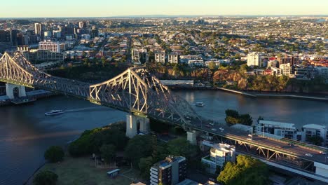 Filmischer-Drohnenüberflug-Und-Rund-Um-Das-Wahrzeichen-Von-Brisbane-City,-Mit-Menschen-Bei-Einem-Abenteuerlichen-Aufstieg-Auf-Die-Story-Bridge-Und-Geschäftigem-Fahrzeugverkehr,-Der-Den-Fluss-Bei-Goldenem-Sonnenuntergang-überquert
