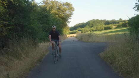 Young-man-riding-a-bicycle-on-a-narrow-rural-road-in-the-countryside