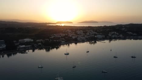 Drone-view-of-coastal-mediterranean-town-with-boats-anchored-with-the-sunrise-in-the-background
