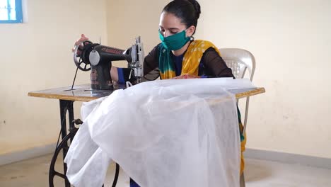 Front-view-of-a-young-beautiful-Indian-girl-operating-a-sewing-machine-to-earn-her-living-wearing-a-mask-for-face-protection-and-mehndi-on-both-her-hands