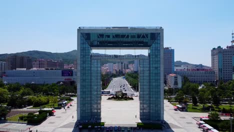 Luftaufnahme-Des-Mächtigen-Xingfu-Tors-Im-Xingfu-Park-In-Der-Stadt-Weihai,-China,-Mit-Blick-Auf-Die-Stark-Befahrene-Straße-Mit-Verkehr-Und-Menschen,-Die-An-Einem-Sommertag-Den-Park-Besuchen