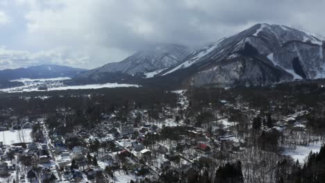 The-drone-captures-the-majestic-grandeur-of-Hakuba-valley-and-the-city-in-Japan-during-winter,-highlighting-the-contrasting-elements-of-snow,-vibrant-forests,-and-thriving-urban-areas