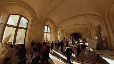 People-touring-looking-at-artwork-sculptures-inside-arched-rooms-of-Louvre-Paris