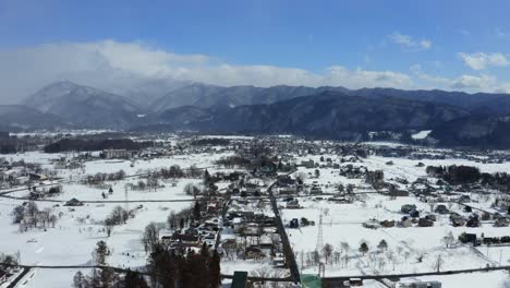 The-drone-soars-gracefully-above-the-breathtaking-Hakuba-valley-and-Hakuba-city-in-Japan,-capturing-the-sweeping-beauty-of-the-winter-landscape-bathed-in-the-warm-glow-of-a-sunny-day