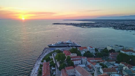 An-aerial-landing-in-sunset-over-Zadar-and-view-over-Adriatic-and-cruise-ship,-over-houses-and-church-of-Saint-Donat-than-Roman-Forum-with-event-going-on