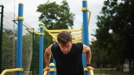 Muscular,-bearded-man-doing-push-ups-on-crossbar-outdoors-on-stadium-in-summer