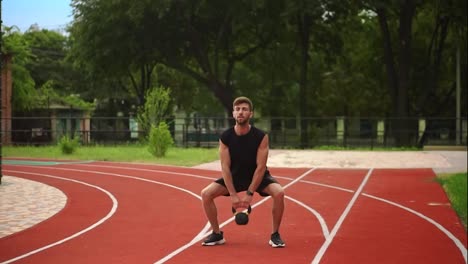 Un-Hombre-Con-Ropa-Deportiva-Negra-Entrena-Con-Peso-Bob-Al-Aire-Libre-Cerca-Del-Estadio-En-La-Pista-De-Carreras