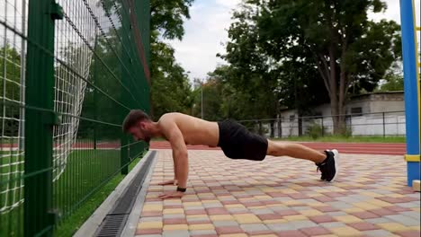 Man-in-black-shorts,-shirtless-doing-push-ups-on-paved-ground-outdoors