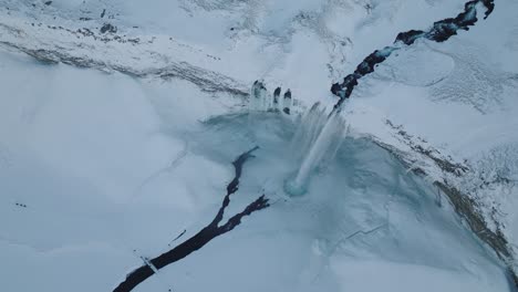 Aerial-panoramic-view-over-a-winter-landscape-covered-in-snow,-over-Seljalandsfoss-waterfall,-in-Iceland,-at-dusk