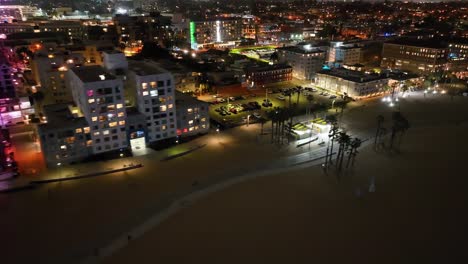 Santa-Monica-beach-front-at-night-down-the-strand-over-the-beach,-aerial-in-the-dark-neighborhood-of-hotels-and-homes