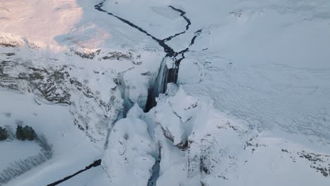 Aerial-view-of-a-winter-landscape-covered-in-snow,-over-Skogafoss-waterfall,-in-Iceland,-at-sunset
