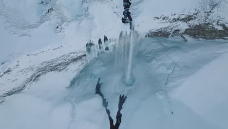 Aerial-top-view-over-a-winter-landscape-covered-in-snow,-over-Seljalandsfoss-waterfall,-in-Iceland,-at-dusk