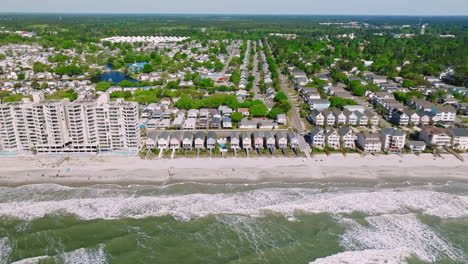 Aerial-flight-over-ocean-showing-colorful-houses-and-apartment-block-at-sandy-Surfside-beach-in-South-Carolina