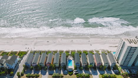 Drone-establishing-shot-of-colorful-hotel-houses-and-swimming-pool-in-front-of-beautiful-surfside-beach-in-South-Carolina-during-sunny-day